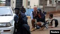 A policeman and photographers take cover after hearing gun shots near the Westgate shopping centre in Nairobi, Sept. 23, 2013. 