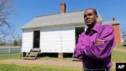 FILE - Rev. Alfred L. Jones III poses in front of the reconstructed slave quarters behind the McLean House on the grounds of Appomattox Court House National Historical Park in Appomattox, Va., April 1, 2015.