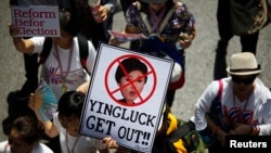 FILE - An anti-government protester carries a placard with a picture of Thai Prime Minister Yingluck Shinawatra as protesters march through central Bangkok, March 29, 2014.