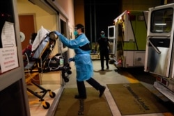 FILE - Emergency medical technician Thomas Hoang, 29, of Emergency Ambulance Service, pushes a gurney into an emergency room to drop off a COVID-19 patient in Placentia, Calif., Jan. 8, 2021.