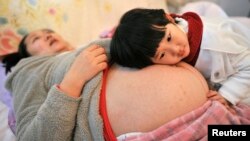두번째 자녀를 가진 중국 안후이성 임산부가 침대에 누워 휴식을 취하는 동안 첫 딸이 배에 귀를 대고 있다. 