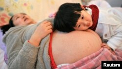 FILE - Li Yan (L), pregnant with her second child, lies on a bed as her daughter places her head on her mother's stomach in Hefei, Anhui province, Feb. 20, 2014. 