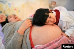 FILE - Li Yan (L), pregnant with her second child, lies on a bed as her daughter places her head on her mother's stomach in Hefei, Anhui province, Feb. 20, 2014.