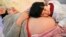 FILE - Li Yan (L), pregnant with her second child, lies on a bed as her daughter places her head on her mother's stomach in Hefei, Anhui province, Feb. 20, 2014. 