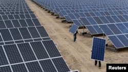 FILE - Employees carry solar panels at a solar power plant in Aksu, Xinjiang Uyghur Autonomous Region, May 18, 2012.