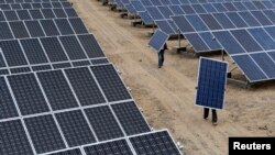 2012年5月18日新疆维吾尔自治区阿克苏市一家太阳能发电厂的员工搬运太阳能电池板