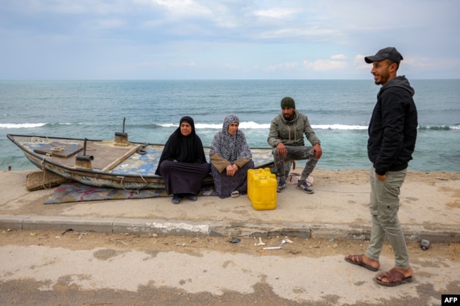 People sit by a beached boat along the Mediterranean seashore at the Shati camp for Palestinian refugees north of Gaza City on Feb. 11, 2025.