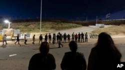 FILE - Migrants are lined up along the border walls separating Tijuana, Mexico, and San Diego, to apply for asylum with U.S authorities, May 7, 2024, in San Diego.