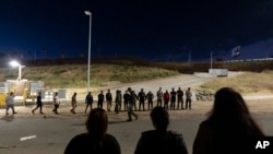 FILE - Migrants line up along the border walls separating Tijuana, Mexico, and San Diego, May 7, 2024. Arrests for illegally crossing the border from Mexico plunged 29% in June to the lowest month of Joe Biden's presidency, according to figures released July 15, 2024, 