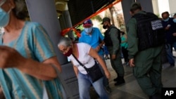 Los residentes pasan por debajo de una tira de cinta adhesiva que sirve como barrera mientras se dirigen a un área donde se les inyectará una segunda dosis de la vacuna Sputnik V COVID-19 en Caracas. Septiembre 21, 2021.