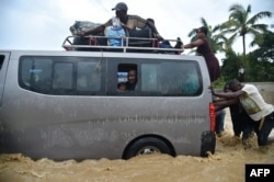 People try to cross the overflowing La Rouyonne river in the commune of Leogane, south of Port-au-Prince, Oct. 5, 2016.