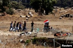 Men ride a motorbike as they carry a Syrian flag in Quneitra on the Syrian side of the cease-fire line between Israel and Syria, as seen from the Israeli-occupied Golan Heights, July 27, 2018.