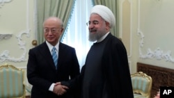 In this photo released by official website of the office of the Iranian Presidency, President Hassan Rouhani, right, and Director General of the International Atomic Energy Agency, IAEA, Yukiya Amano shake hands for media at the start of their meeting at 