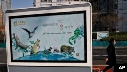 Una mujer con mascarilla camina frente a un póster que promueve a los animales silvestres como amigos en lugar de alimento, después que las autoridades chinas prohibieron los mercados de animales en Beijing. Marzo 11 de 2020.