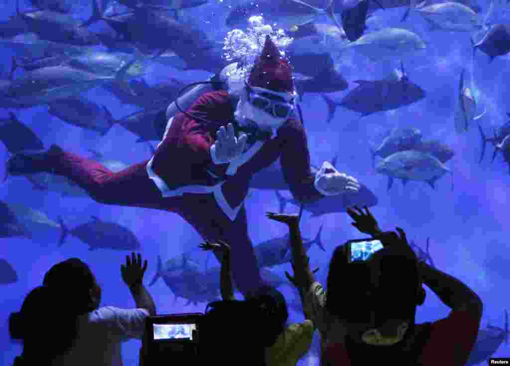 Para pengunjung melambai kepada penyelam yang memakai seragam Santa Claus di sebuah taman wisata aquarium di Manila, Filipina.