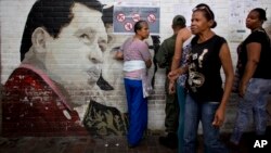 Personas buscan sus nombres en el padrón electoral cerca de un mural dedicado a Hugo Chávez, el domingo, durante las elecciones municipales en Caracas.