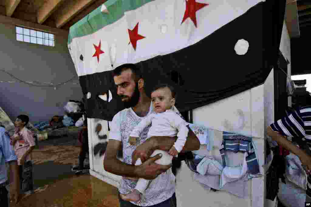 A Syrian man, who fled his home due to government shelling, holds his son at Bab Al-Salameh border crossing, hoping to cross to a refugee camps in Turkey, near the Syrian town Azaz, September 12, 2012. 