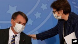 Brazil's President Jair Bolsonaro wearing a protective mask to curb the spread of the new coronavirus, left, talks with Agriculture Minister Tereza Cristina during the launching ceremony of a rights guarantee program for rural women, at the Planalto…