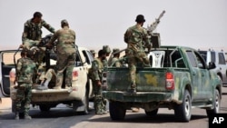 FILE - This photo released Sept 4, 2017, by the Syrian official news agency SANA shows Syrian troops and pro-government gunmen standing on pickup trucks with heavy machine guns mounted on them, in the eastern city of Deir el-Zour, Syria.