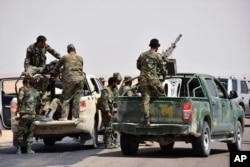 FILE - This photo released Sept 4, 2017, by the Syrian official news agency SANA shows Syrian troops and pro-government gunmen standing on pickup trucks with heavy machine guns mounted on them, in the eastern city of Deir el-Zour.