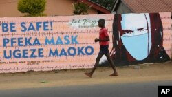 A young boy walks past a wall with graffiti urging people to wear face masks in Harare, May, 28, 2020. Manhunts have begun after hundreds of people fled quarantine centers in Zimbabwe and Malawi.