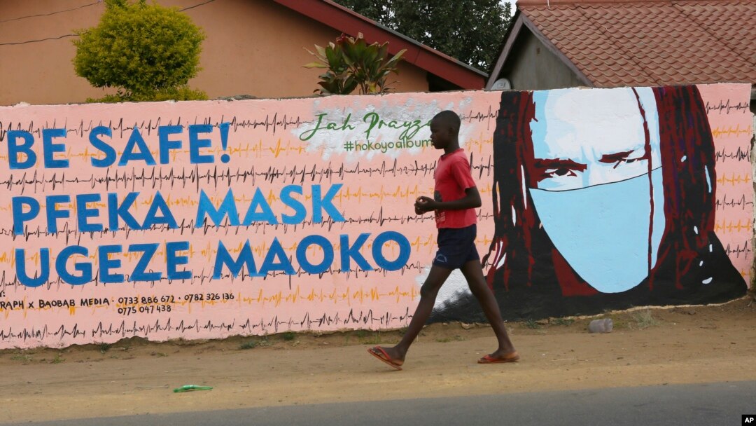 A young boy walks past a wall with graffiti urging people to wear face masks in Harare, May, 28, 2020. Manhunts have begun after hundreds of people fled quarantine centers in Zimbabwe and Malawi.