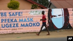 A young boy walks past a wall with graffiti urging people to wear face masks in Harare, May, 28, 2020. Manhunts have begun after hundreds of people fled quarantine centers in Zimbabwe and Malawi.