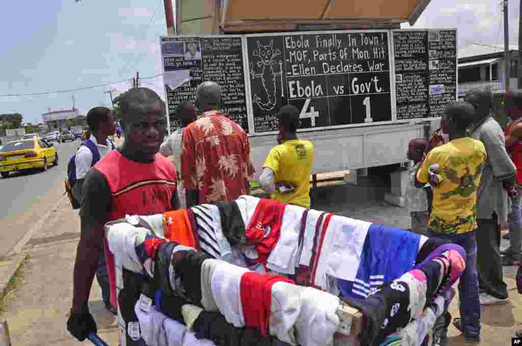 A man sells clothes as he walks past people reading comments on a blackboard that informs the public of&nbsp;current events in Liberia, including information on the Ebola virus, in Monrovia, Liberia, Saturday Aug. 2, 2014.&nbsp;