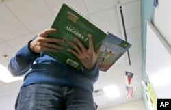 A student holds an Algebra textbook.