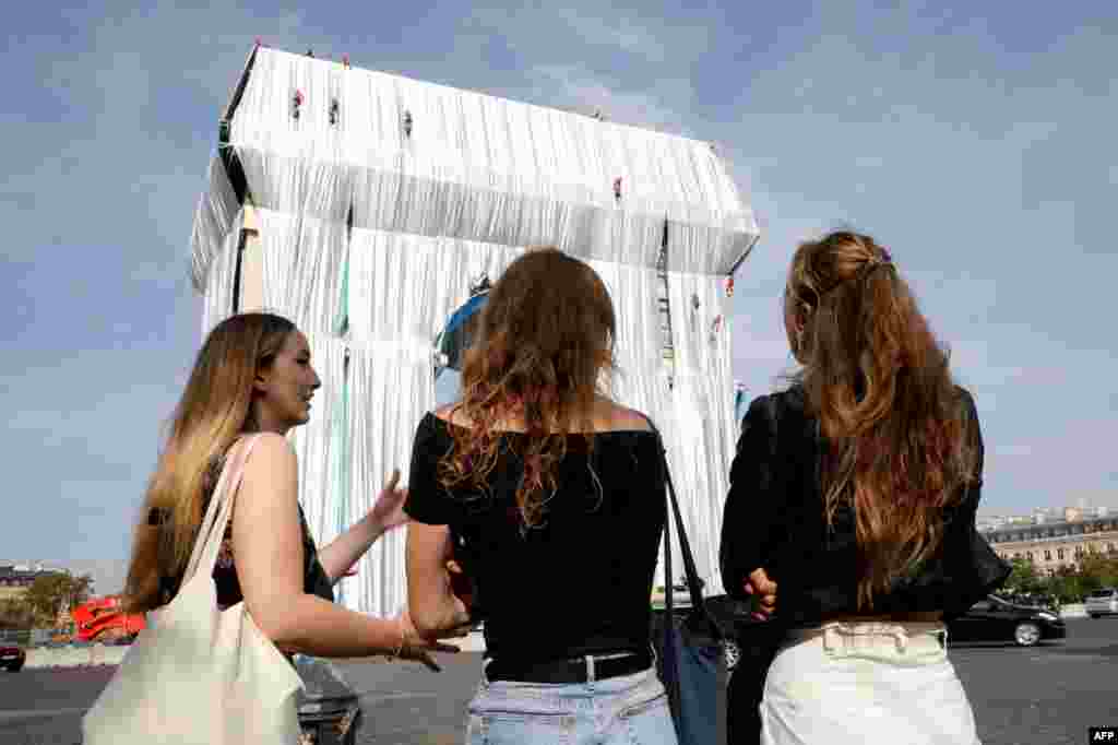 Bystanders look on as workers arrange silver blue fabric, part of a process of wrapping L&#39;Arc de Triomphe in Paris, France, designed by the late artist Christo.