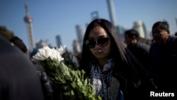 A woman offers flowers during a memorial ceremony in memory of people who were killed in a stampede incident during a New Year's celebration, on the Bund in Shanghai, Jan. 1, 2015. 