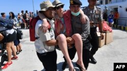Seorang turis asing yang dievakuasi dari Pulau Gili Trawangan sedang dibantu saat tiba di pelabuhan di Bangsal, di utara Lombok, Selasa, 7 Agustus 2018. (Foto: AFP)
