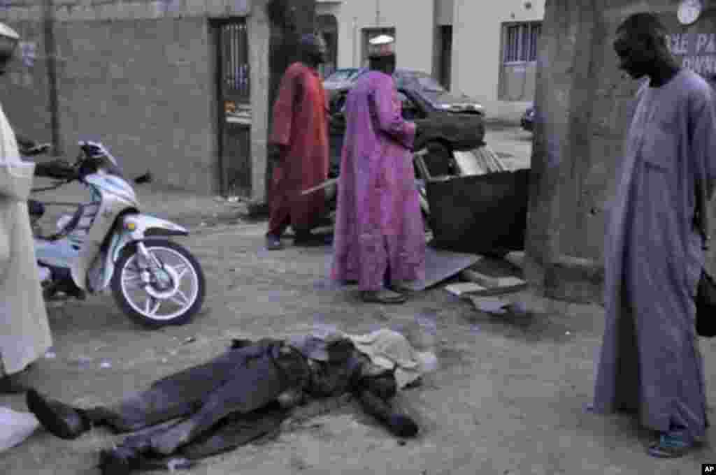 People look at the body of an unidentified immigration officer after an explosion near the immigration office in Nigeria's northern city of Kano January 20, 2012.