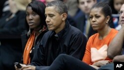 FILE - President Barack Obama, with first lady Michelle Obama at his left, checks his BlackBerry as they watch a basketball game in Towson, Maryland, Nov. 26, 2011.