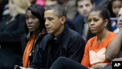 Presiden Barack Obama, di samping ibu negara Michelle Obama, mengecek BlackBerrynya ketika menonton pertandingan bola basket di Towson, Maryland, 26 November 2011. (Foto: dok.)