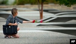 FILE - A woman reaches out to touch rose on one of the benches of the Pentagon Memorial at the at the Pentagon, Sept. 11, 2014.
