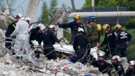 In this Monday, July 5, 2021, file photo, rescue workers move a stretcher containing recovered remains at the site of the collapsed Champlain Towers South condo building, in Surfside, Fla. (AP Photo/Lynne Sladky, File)