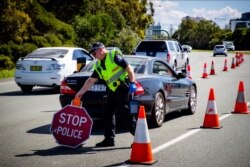 FILE - A Queensland police officer moves a stop sign at a vehicle checkpoint on the Pacific Highway on the Queensland - New South Wales border, in Brisbane, Apr. 5, 2020.