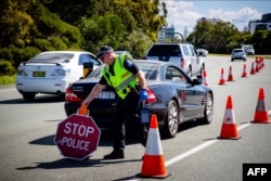 FILE - A Queensland police officer moves a stop sign at a vehicle checkpoint on the Pacific Highway on the Queensland - New South Wales border, in Brisbane, Apr. 5, 2020.