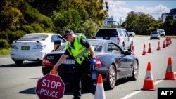 FILE - A Queensland police officer moves a stop sign at a vehicle checkpoint on the Pacific Highway on the Queensland - New South Wales border, in Brisbane on April 15, 2020. 
