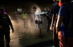 A man who was detained for not complying with COVID-19 regulations by breaking curfew and being out on the street drinking is disinfected with an alcohol solution in Caracas, Venezuela, on Aug. 8, 2020.