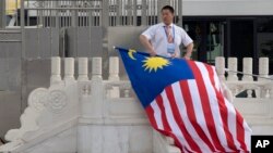 FILE - A worker rolls up a Malaysian national flag after the arrival of the Malaysian delegation at Beijing's International Airport ahead of a Belt and Road forum in Beijing, China, May 12, 2017.