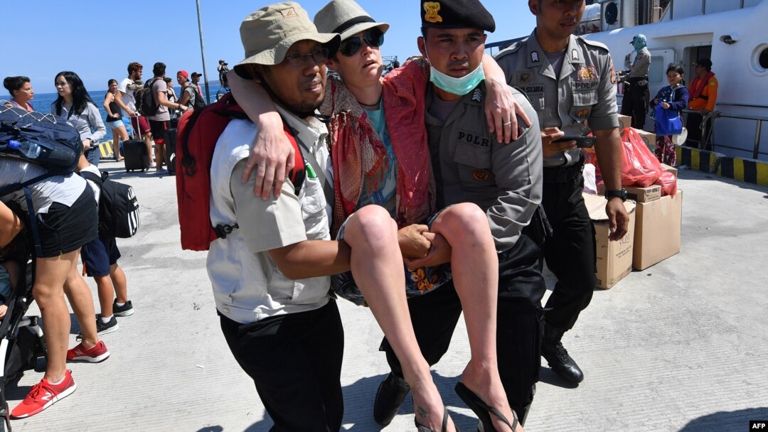 Seorang turis asing yang dievakuasi dari Pulau Gili Trawangan sedang dibantu saat tiba di pelabuhan di Bangsal, di utara Lombok, Selasa, 7 Agustus 2018. (Foto: AFP)
