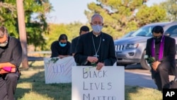 In this June 1, 2020, photo provided by the Catholic Diocese of El Paso, Bishop Mark Seitz, center, kneels with other demonstrators at Memorial Park holding a Black Lives Matter sign in El Paso, Texas. 