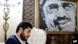 FILE - Abdullah Morsi, the youngest son of Egypt's former President Mohamed Morsi, sits in front of a framed image of his father that was printed on a flag during the 2013 Rabaah al-Adawiya sit-in, at his home in Cairo, Egypt.