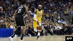 LeBron James of the Los Angeles Lakers (R) drives the ball in front of Wilson Chandler of the Brooklyn Nets (L) during the National Basketball Association (NBA) pre-season match between the LA Lakers and Brooklyn Nets at the Mercedes Benz Arena in Shanghai.