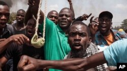 A Burkina Faso protestor holds a loaded slingshot as others gesture, in the city of Ouagadougou, Burkina Faso, Thursday, Sept. 17, 2015. While gunfire rang out in the streets, Burkina Faso’s military took to the airwaves Thursday to declare it now controls the West African country, confirming that a coup had taken place just weeks before elections. (AP Photo/Theo Renaut)