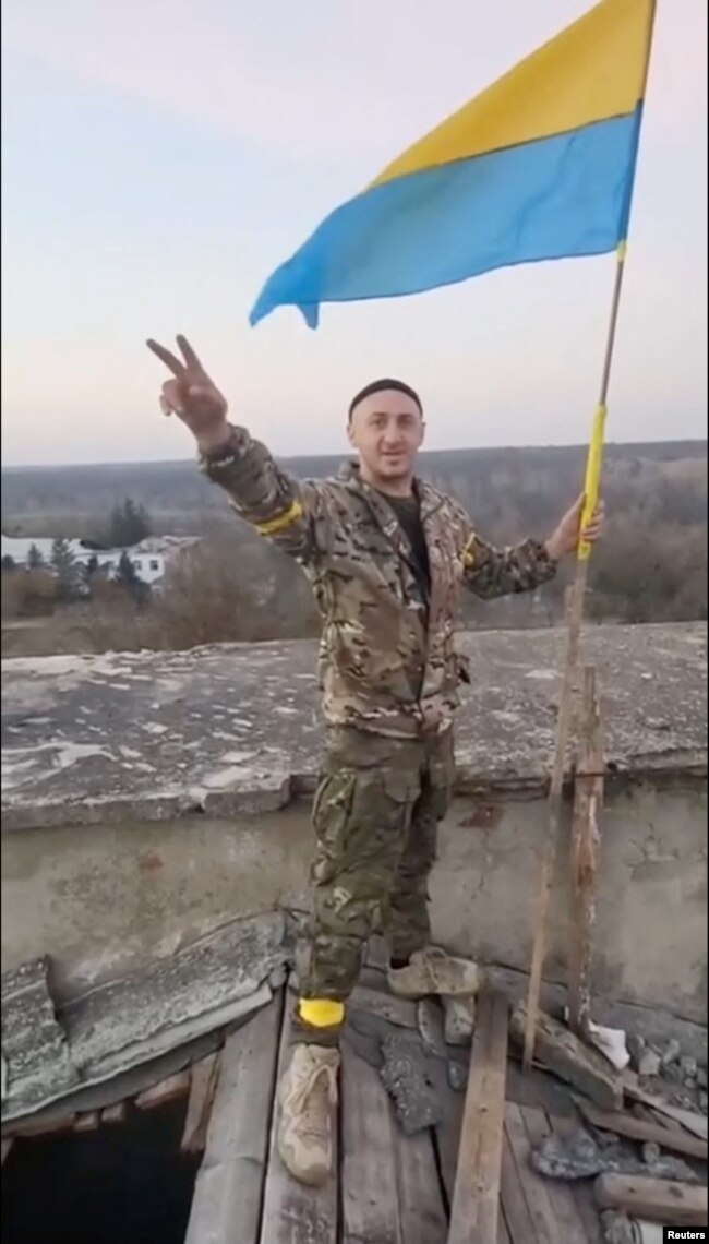一名身穿军装的男子在乌克兰赫尔松地区手举国旗打出胜利的手势。（2022年11月9日）