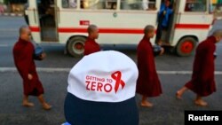 Logo tampak di topi seorang wanita yang berdiri dekat biksu Budha yang berjalan untuk mengumpulkan derma, selama pawai peringatan Hari AIDS Sedunia 2013 di Kandawgyi, Yangon (foto: REUTERS/Soe Zeya)