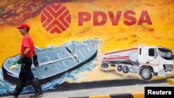 Un empleado de una estación de servicio de Caracas pasa frente a un mural con el logo de la estatal petrolera PDVSA, en agosto de 2014.